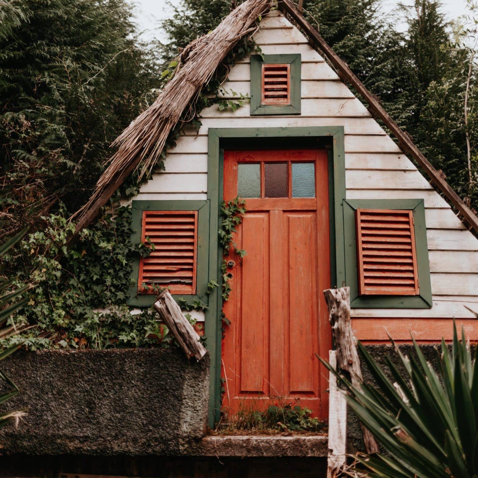 A triangular wooden hut stands in the middle of the forest.