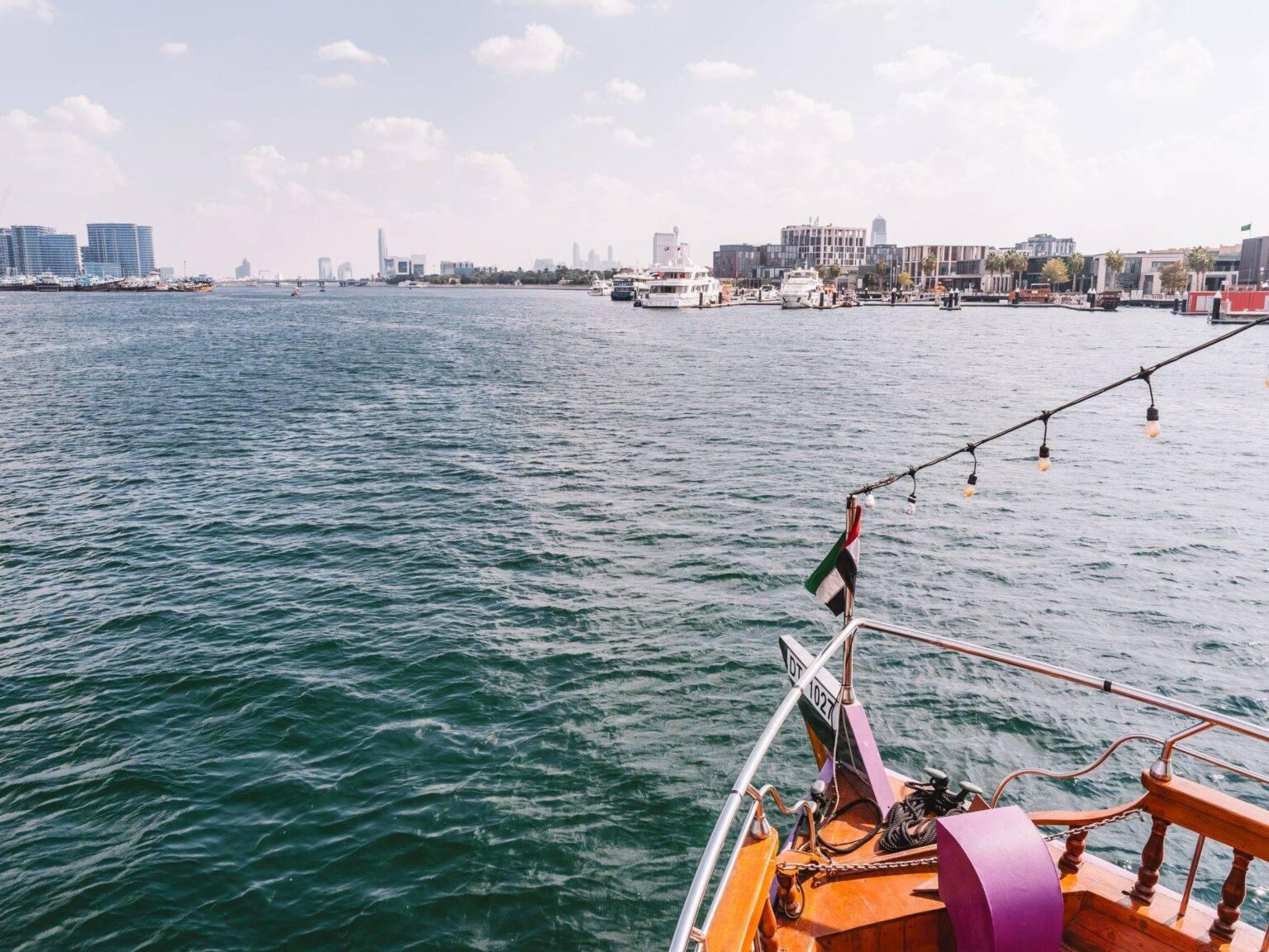 La proa de un barco en el Dubai Creek con otros barcos y rascacielos al fondo.