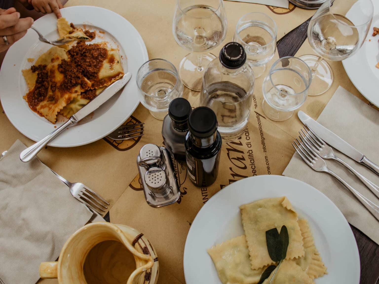 Una mesa puesta con especialidades de pasta italiana en platos blancos, acompañada de vino blanco italiano.