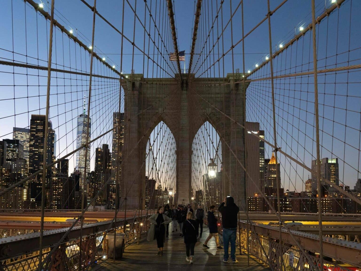 The Brooklyn Bridge at night with the illuminated skyline in the background.