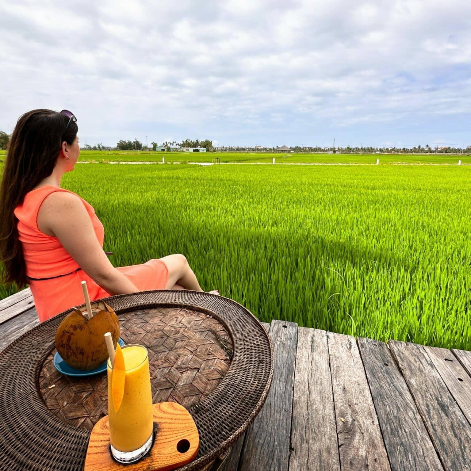 Biggi sits on a platform in front of the green rice fields.