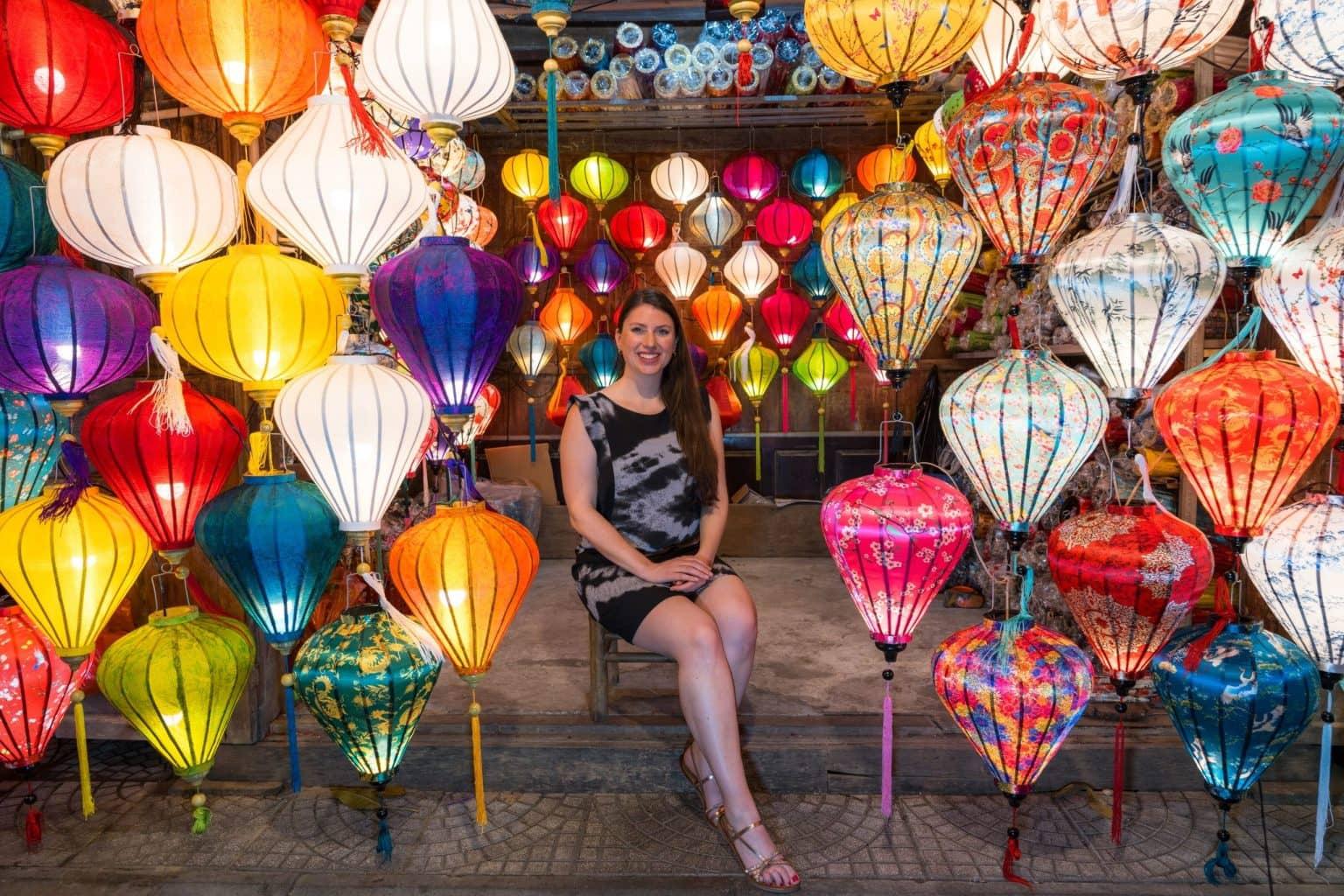 The blogger sits between many colorful lanterns.