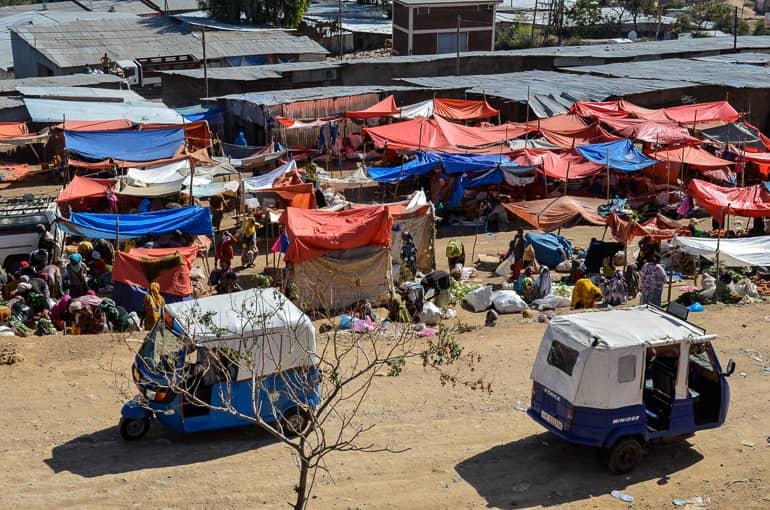 At a spice market in Harar, Ethiopia, red and blue tarps protect the stalls from the sun as two small delivery vans cross the path.