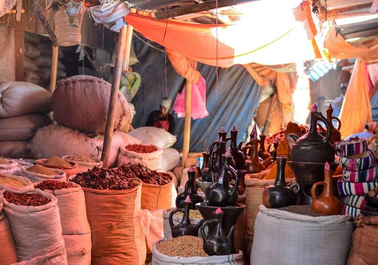 On a marketplace in Harar, Ethiopia, spices are sold in large bags and oils in clay jugs under fabric sails.