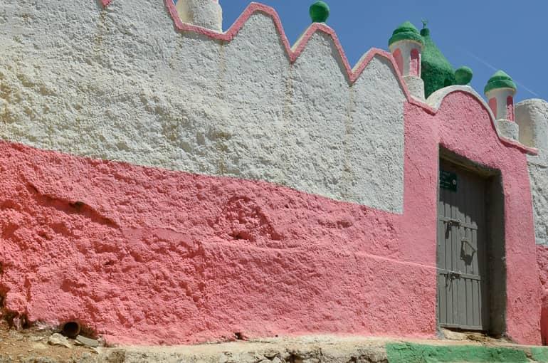 The wavy facade of a mosque in white and pink with green towers in Harar, Ethiopia.