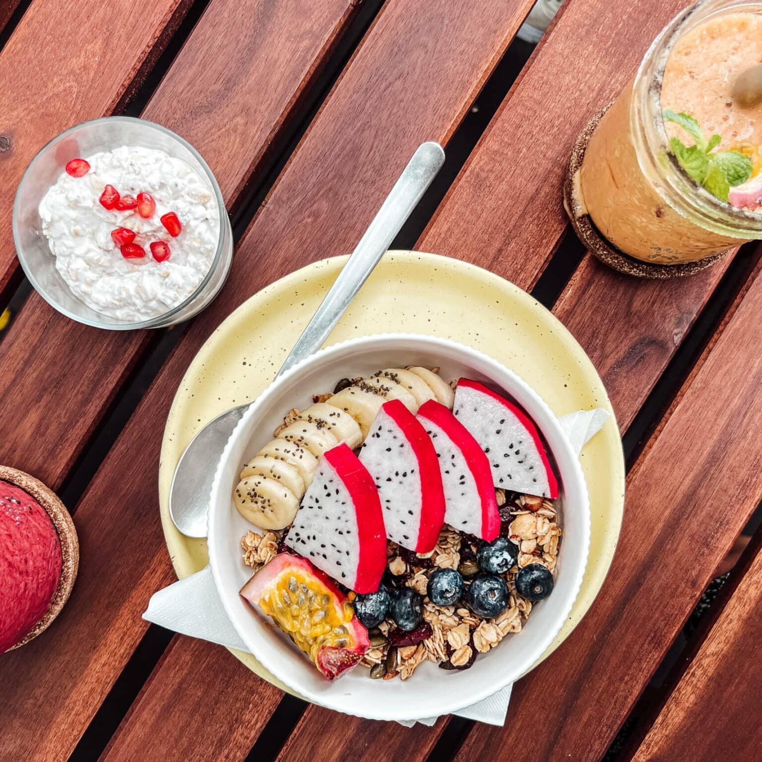 An acai bowl and two smoothies sit on a wooden table.