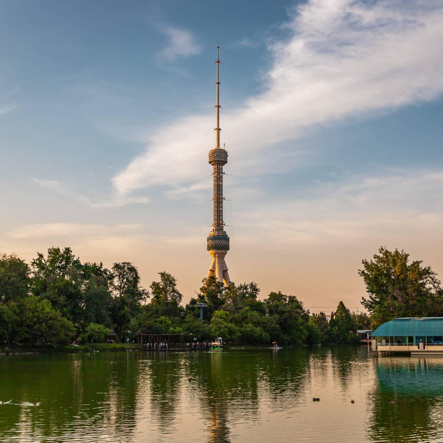 The Tashkent TV Tower reflected in a lake, surrounded by green trees