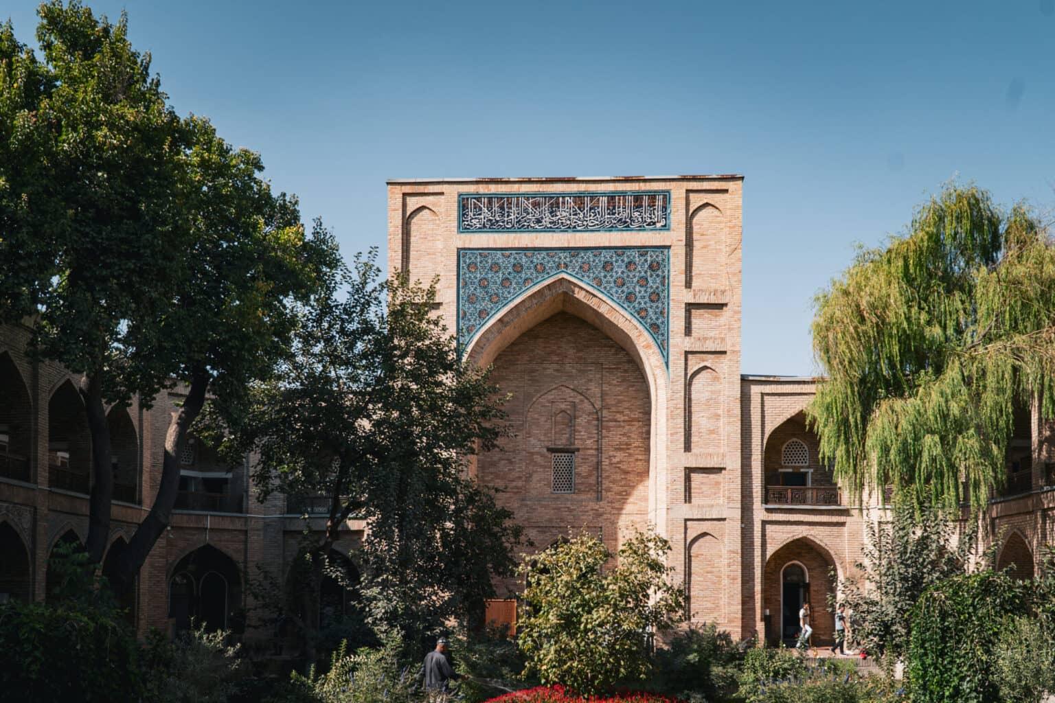 Exterior view of the Ko'kaldosh Madrasa in Tashkent with decorated arches in a garden