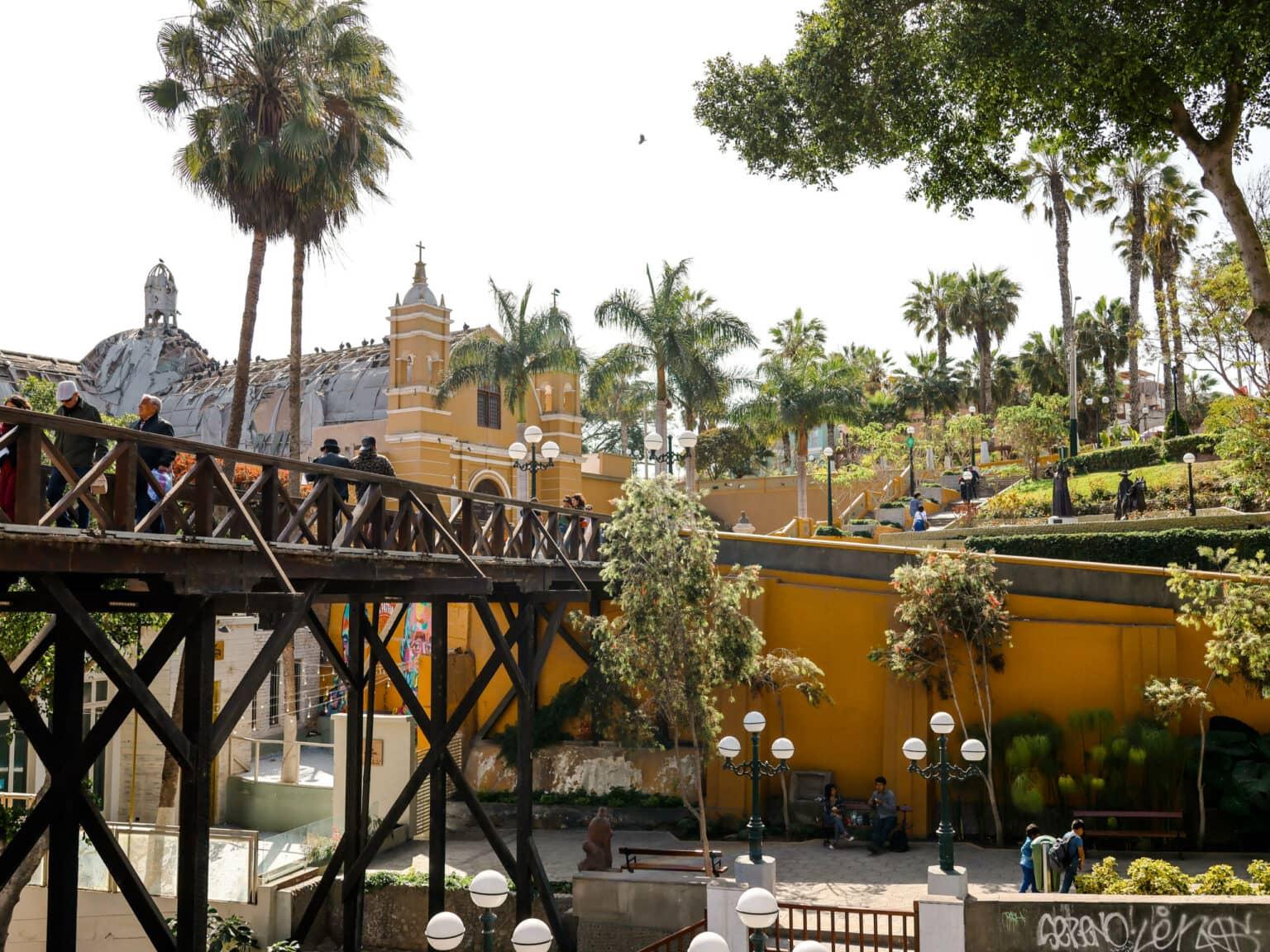Amid palm trees stands the sigh bridge, made of dark wood, in Lima.