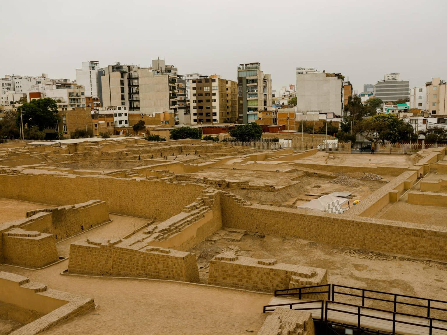 An old sand-colored ruin in the midst of the city of Lima, surrounded by residential buildings.