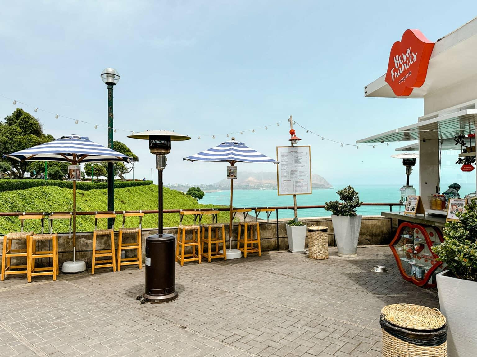 A small café on Lima's coastal promenade with blue and white umbrellas and a view of the sea.