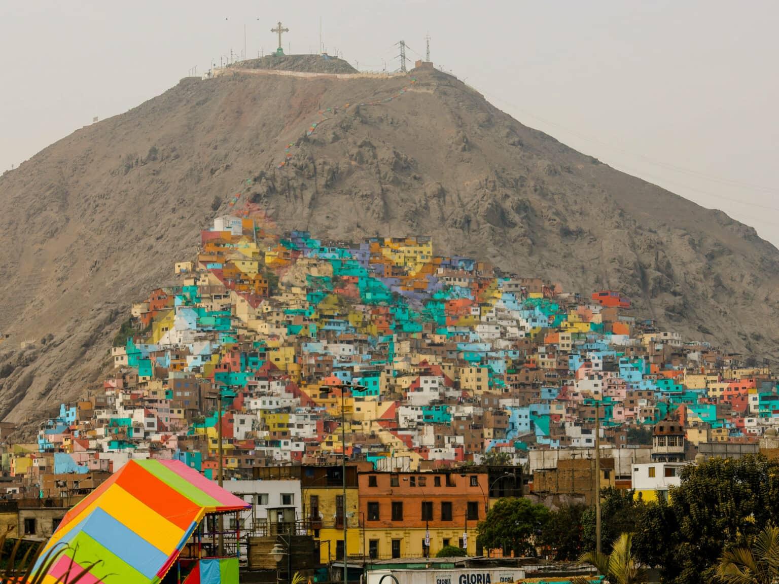 A gray mountain is climbed by colorful house buildings.