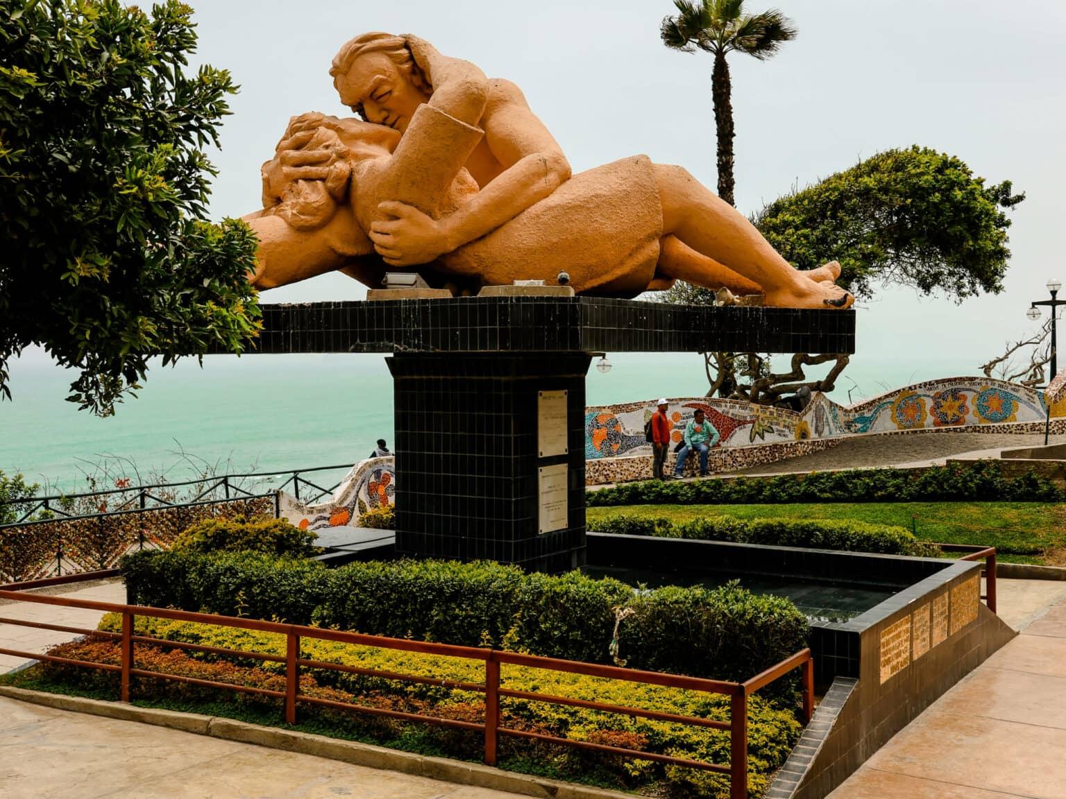 A statue of two kissing people in Lima's Park of Lovers with turquoise sea in the background.