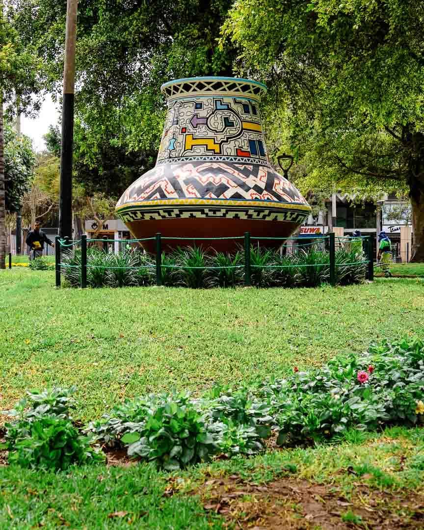 A lush green meadow in Kennedy Park in Lima adorned with a gigantic clay vase made of colorful mosaic pieces.