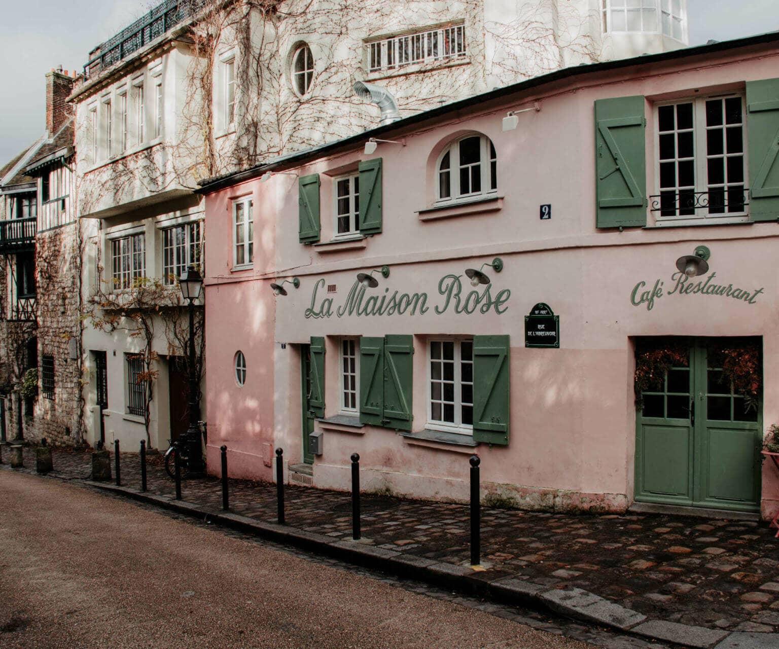 La Maison Rose es un café y restaurante parisino en una pequeña calle con fachada rosa y contraventanas verdes.