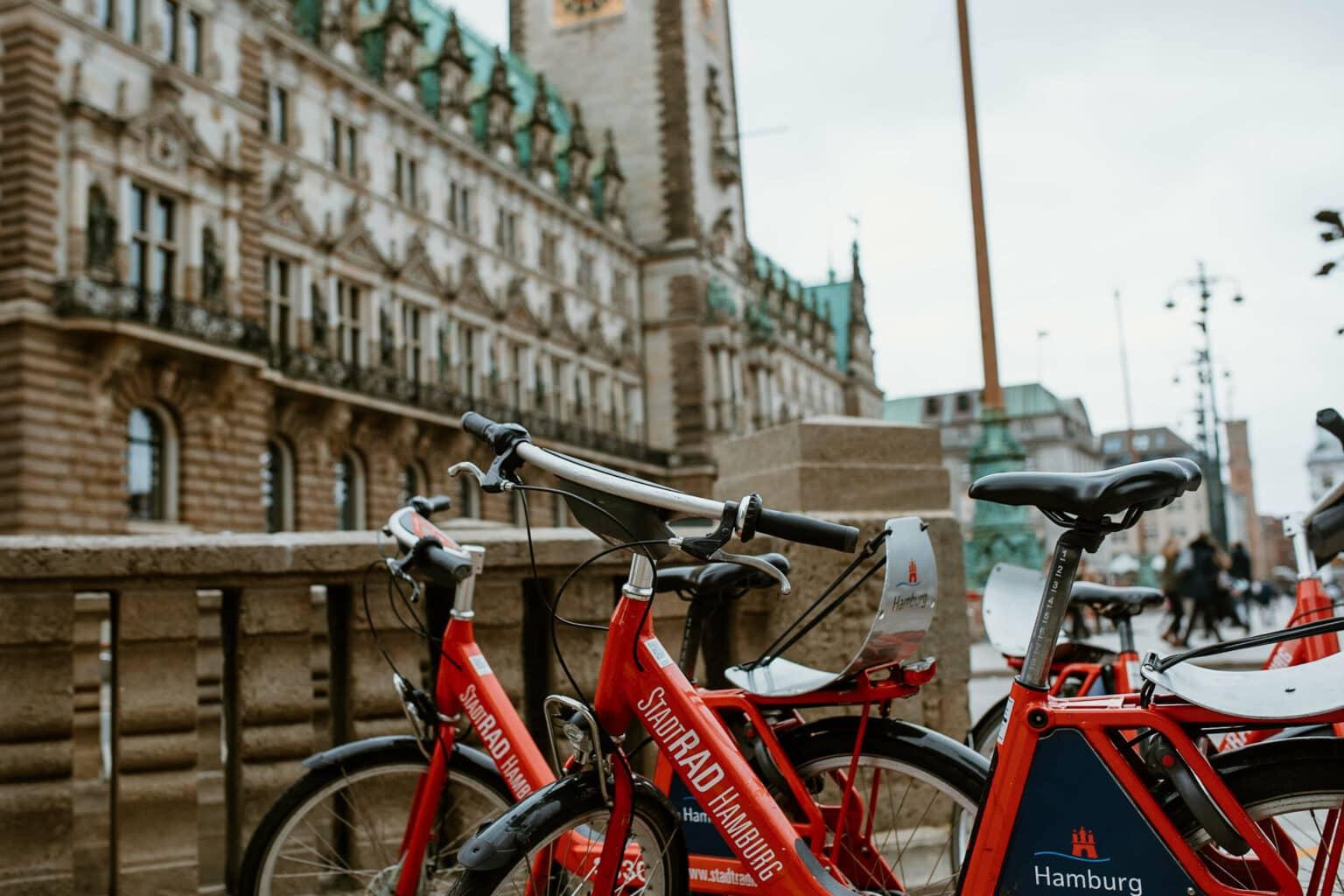 Two red bicycles from the provider 'StadtRad' stand in front of the Town Hall in Hamburg.