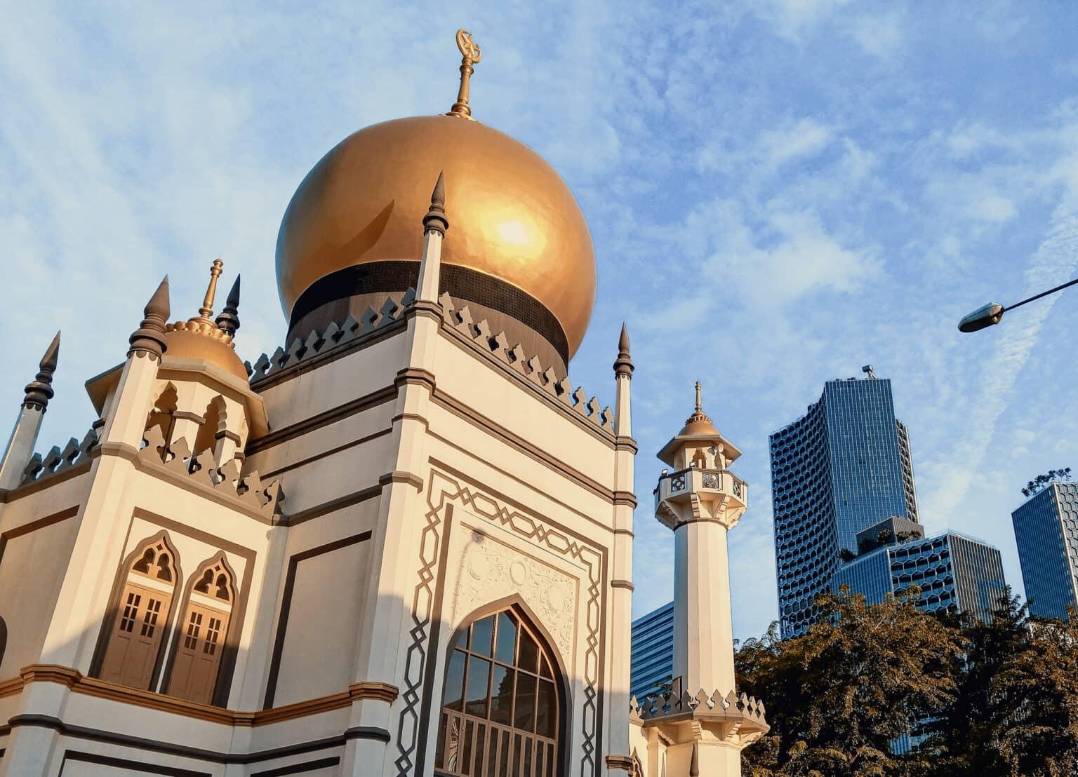 La mezquita Sultan en el barrio de Kampong Glam en Singapur con su cúpula dorada y rascacielos al fondo.