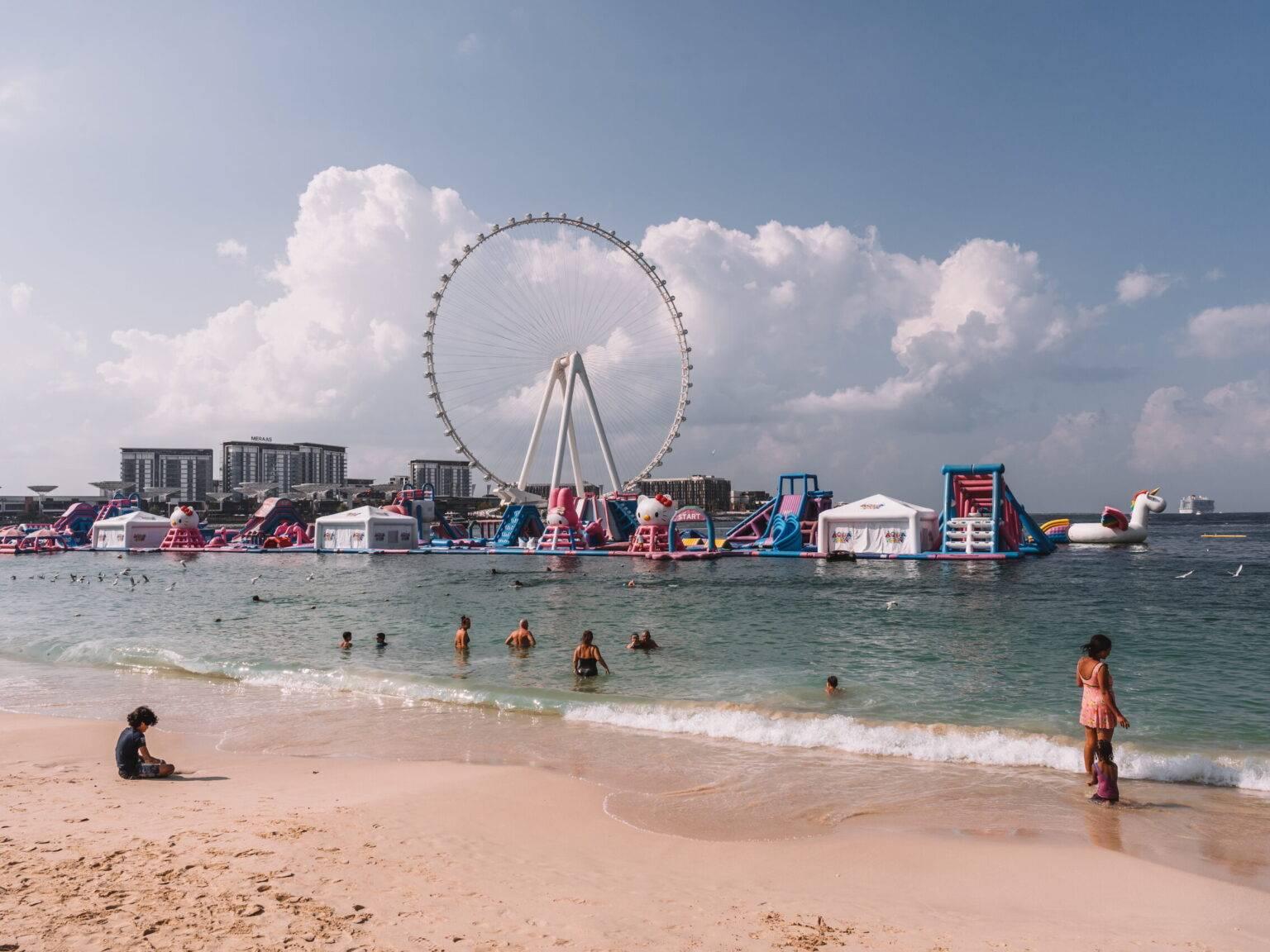 Some people in the sea at JBR Beach in Dubai with inflatables and a Ferris wheel in the background.