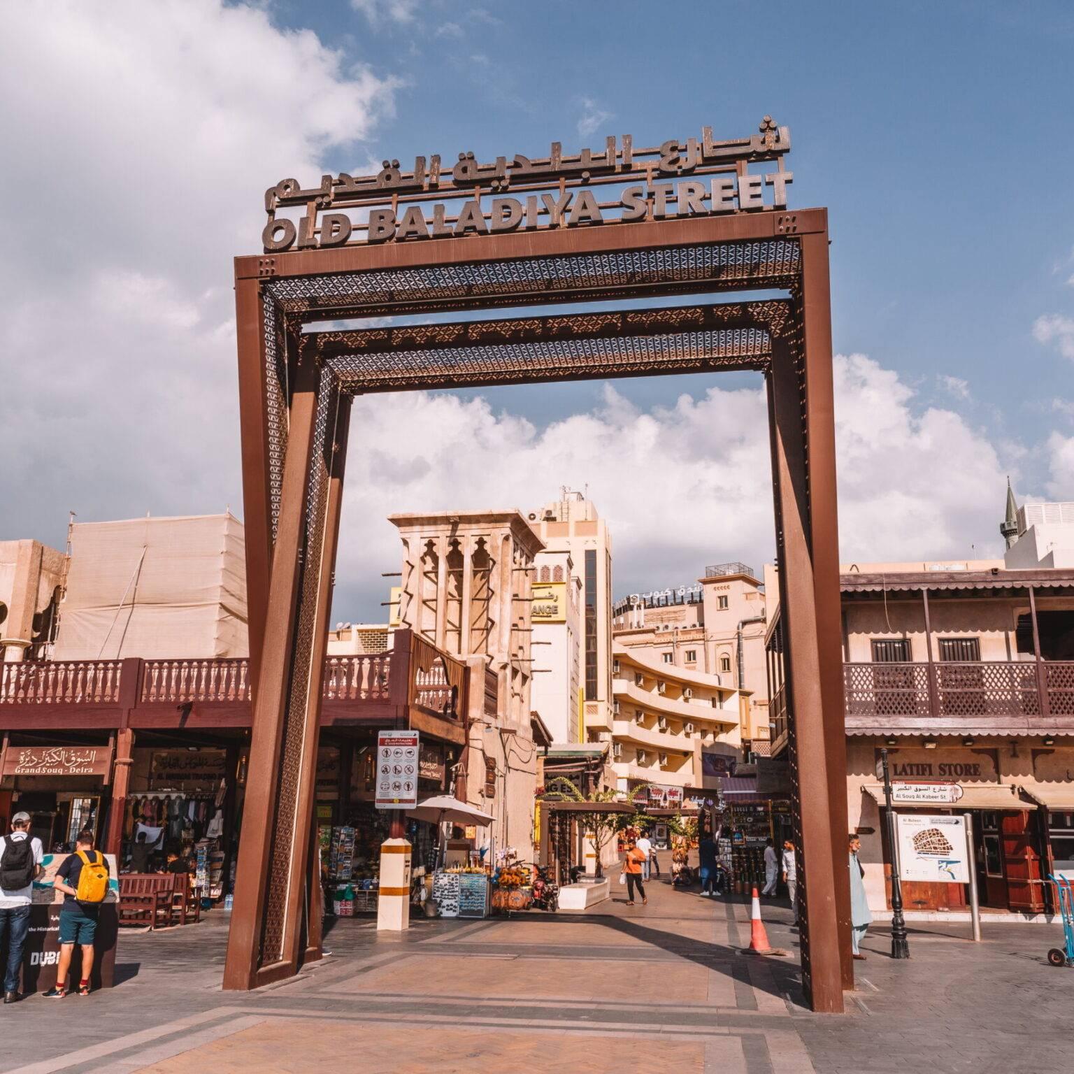 A large metal gate with the inscription "OLD BALADIYA STREET" with some buildings in the background.