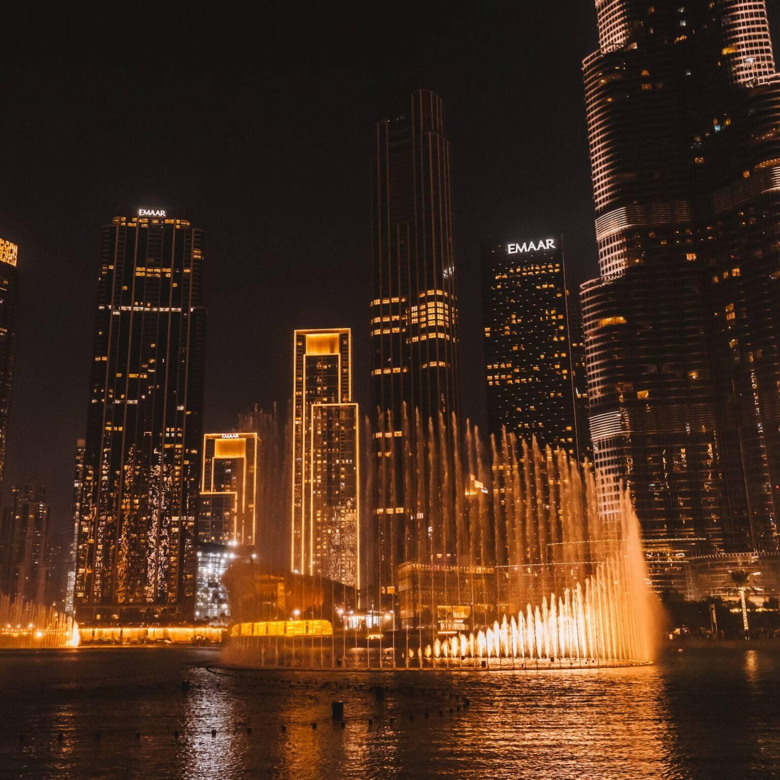 The Dubai Fountains at night surrounded by illuminated skyscrapers.