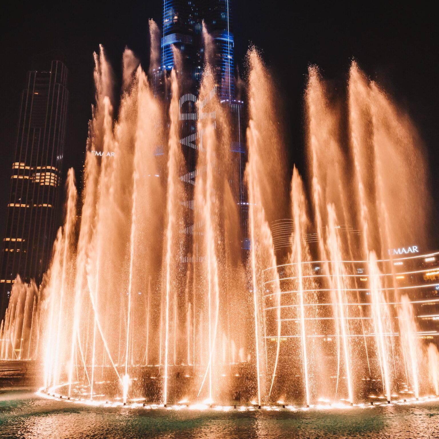 The Dubai Fountains at night surrounded by illuminated skyscrapers.