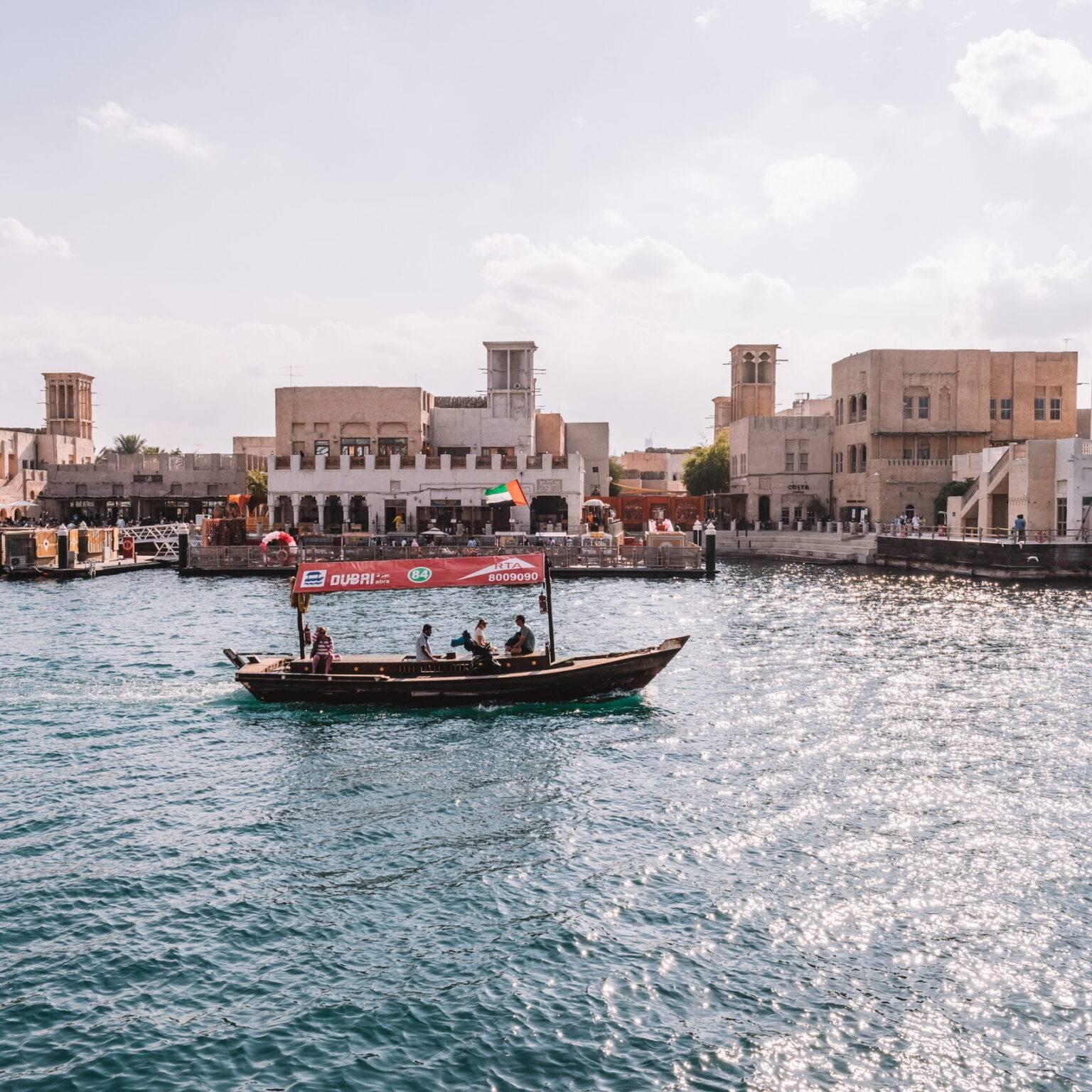 A small covered boat on a river with some buildings in the background.