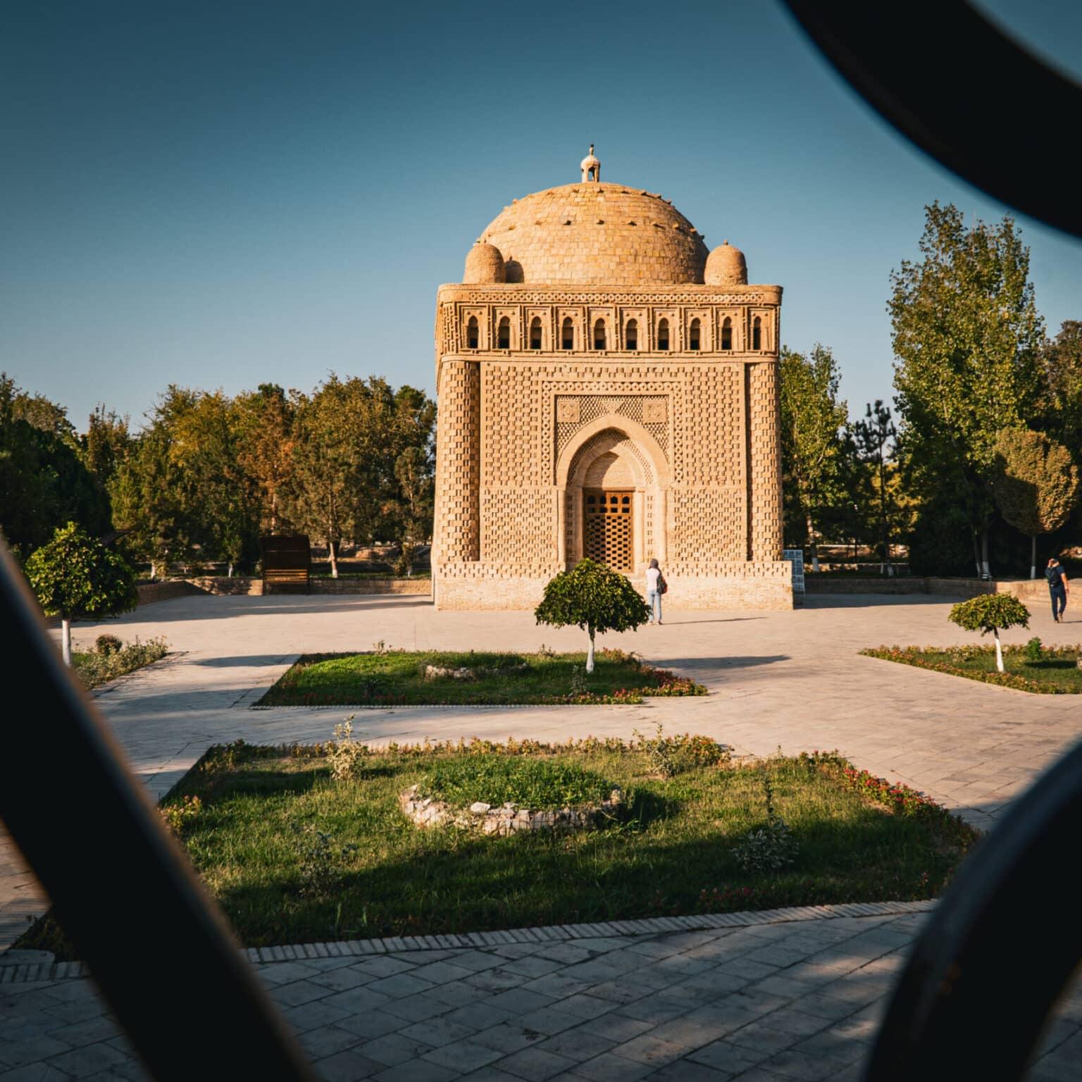 The Samanid Mausoleum in Bukhara with brick architecture, set in a green park illuminated by afternoon light