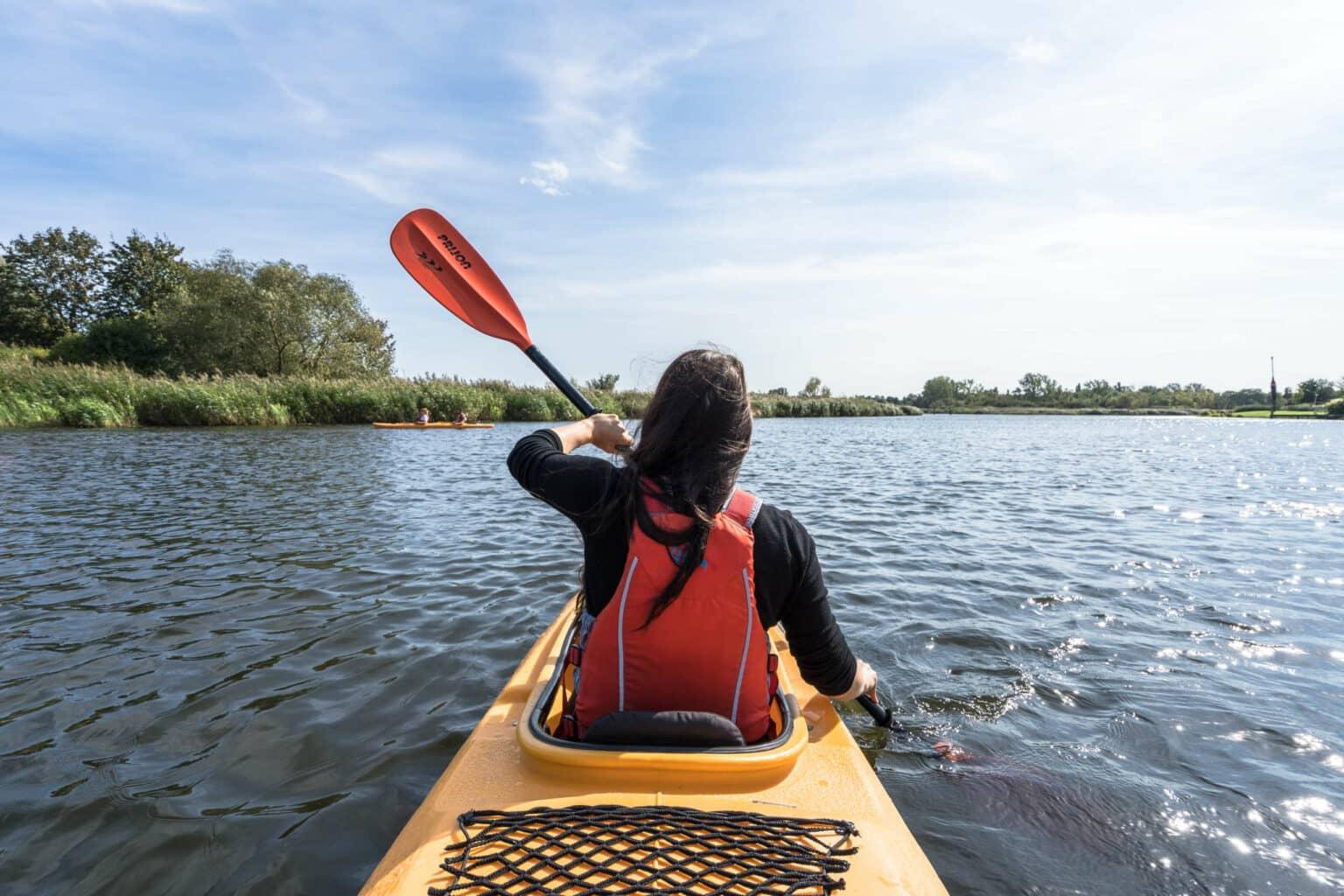 Blogger Biggi from Phototravellers paddles in a yellow kayak on the Warnow River near Rostock.