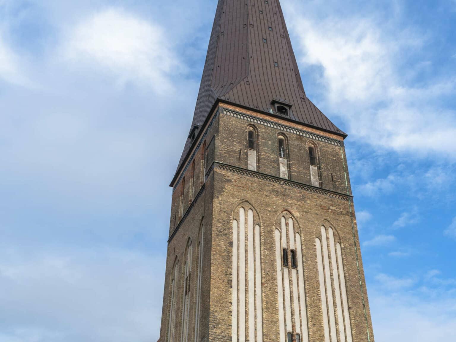 The Rostock St. Peter's Church rises into the radiant blue sky with white clouds, the brown bricks can be seen from a frog's perspective.