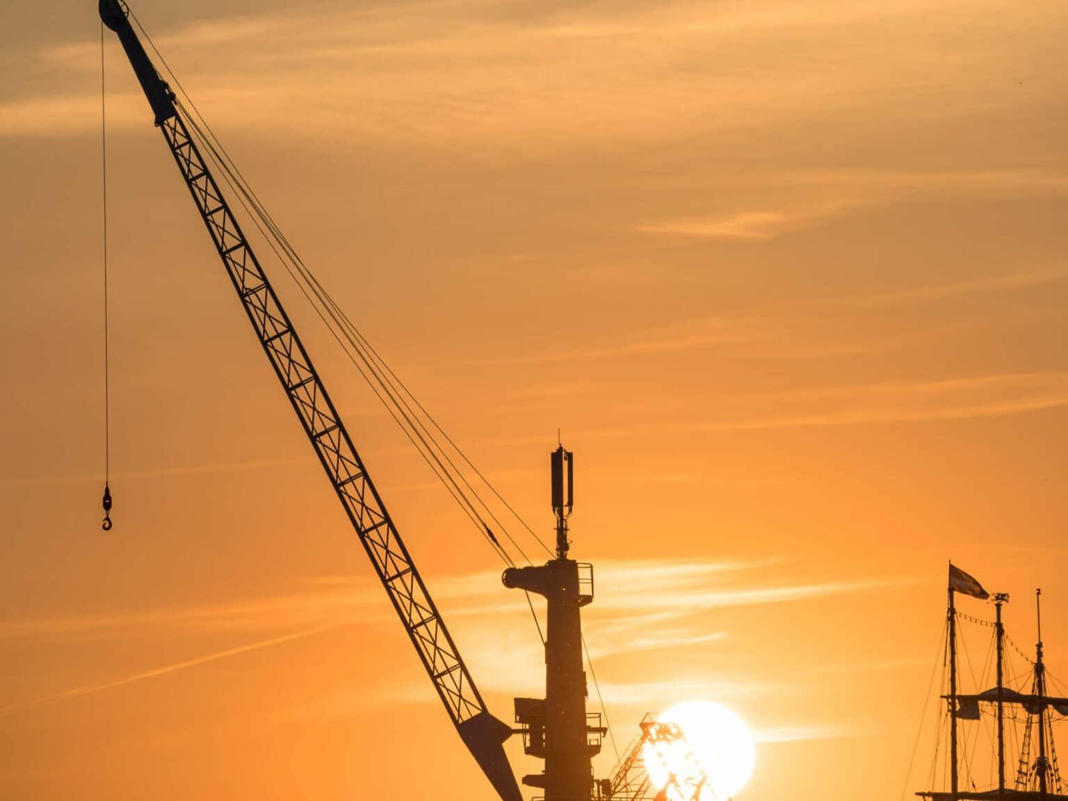An old crane in Rostock's harbor illuminated by the setting sun, the sky is completely orange, casting its light on the crane.