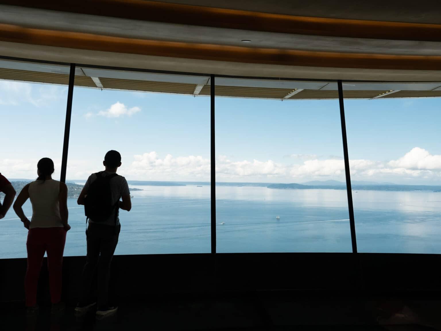 A few people stand in front of the panoramic windows of the Space Needle.