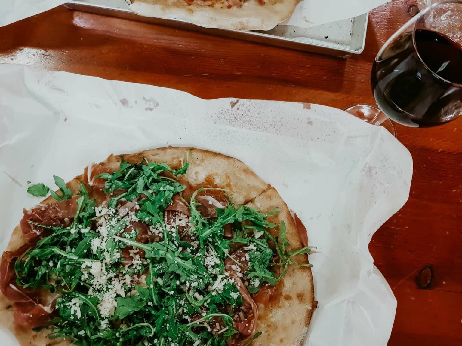 A pizza with a glass of red wine next to it.