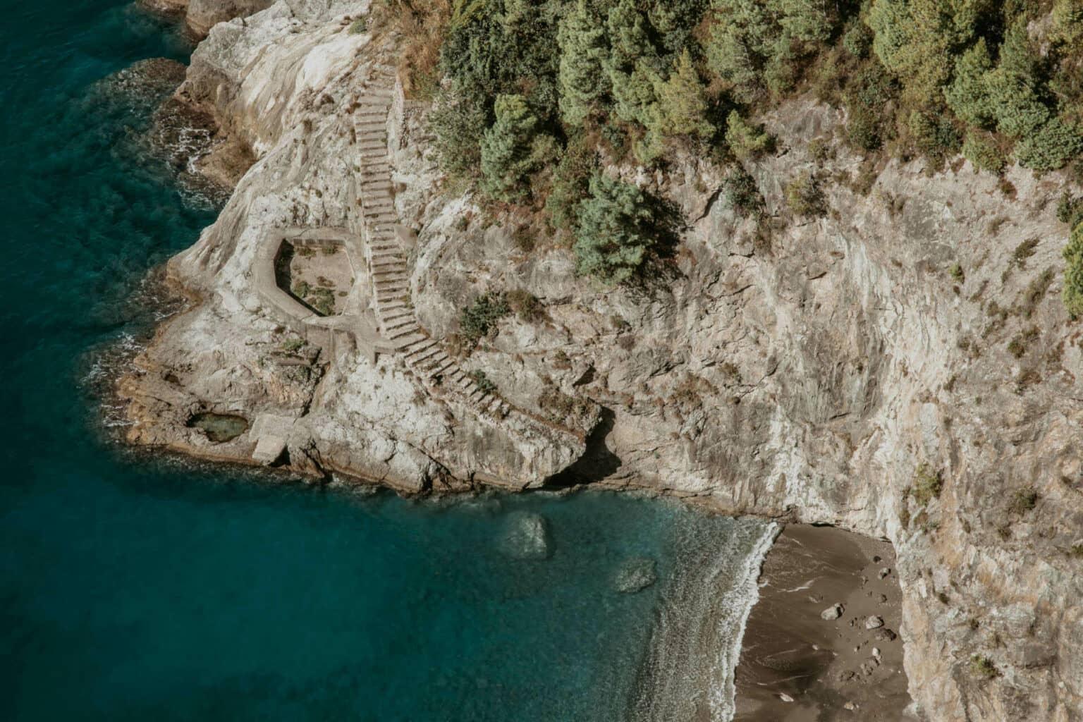A small beach seen from above, with a long staircase leading down from the mountain.