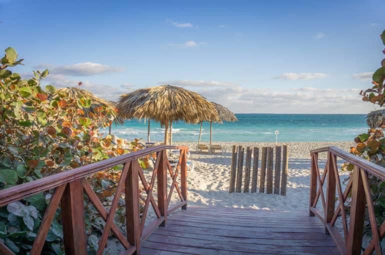 Un pequeño muelle conduce a la playa de arena blanca y mar turquesa en Varadero, pequeñas sombrillas de paja protegen del sol.
