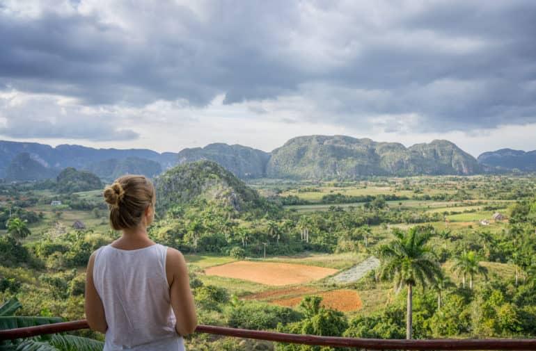 Una mujer mira de espaldas a la cámara hacia el paisaje que rodea Viñales, Cuba, lleno de palmeras y colinas.
