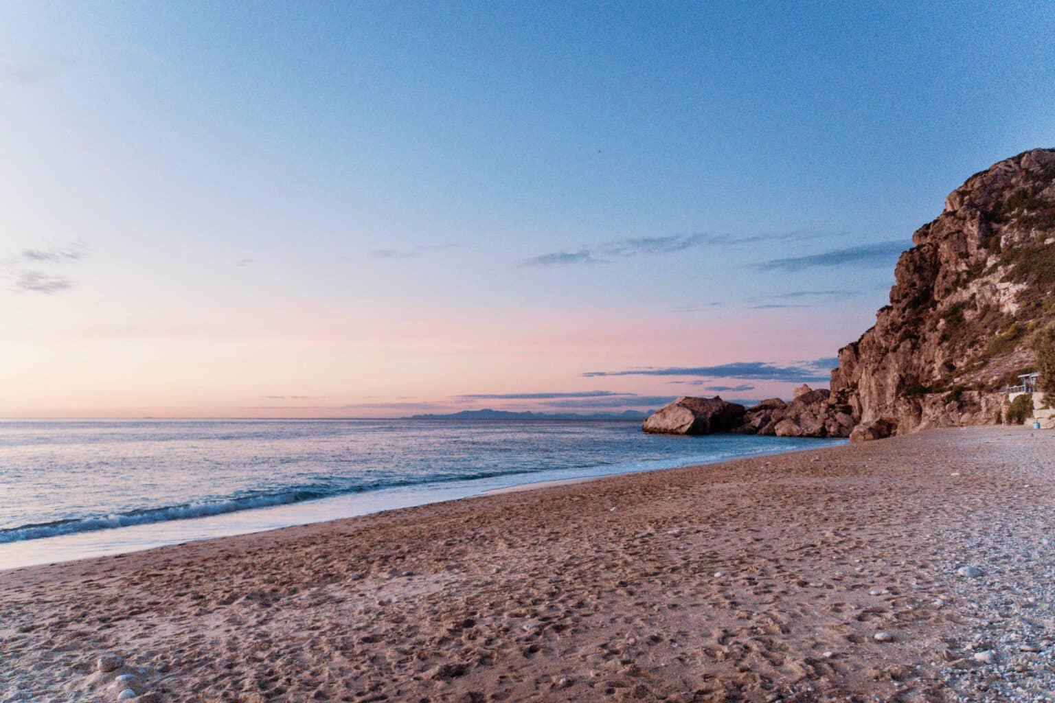The light of the setting sun bathes Kathisma Beach in Lefkada, the calm sea, and the sky in soft colors.