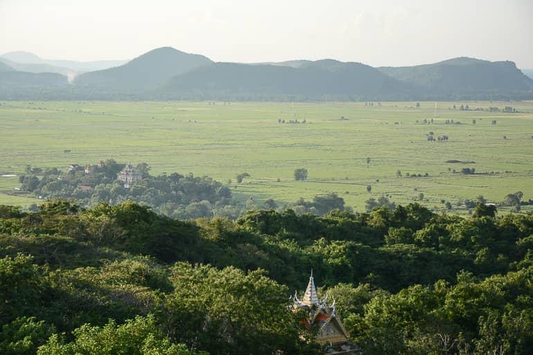 From the summit of Phnom Sampov in Battambang, Cambodia, the view extends over forests, endless green fields, and overgrown hills.