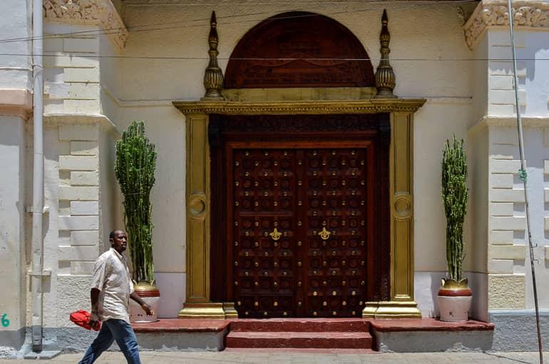 Una puerta decorada de madera oscura con marco dorado adorna la entrada de una casa en Zanzíbar.