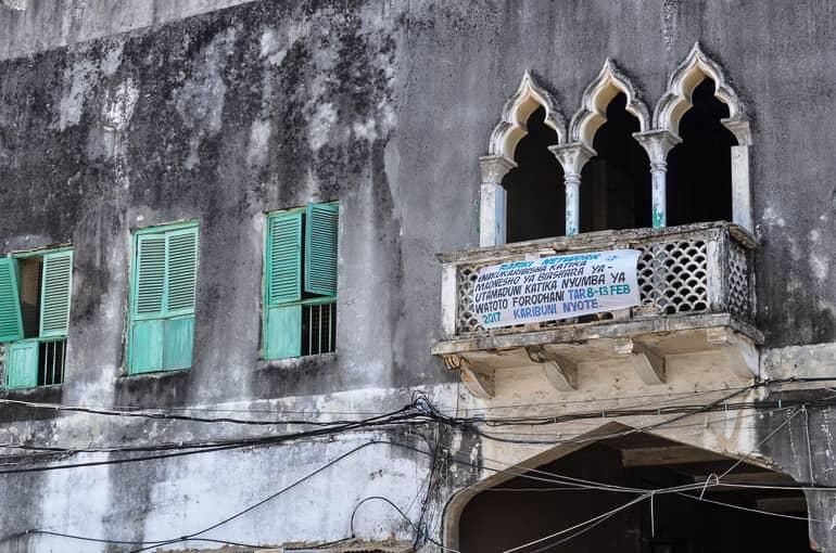Una fachada de casa en mal estado en Zanzíbar sugiere influencia india, con persianas verdes parcialmente rotas y muchos cables corriendo desordenadamente por la fachada.