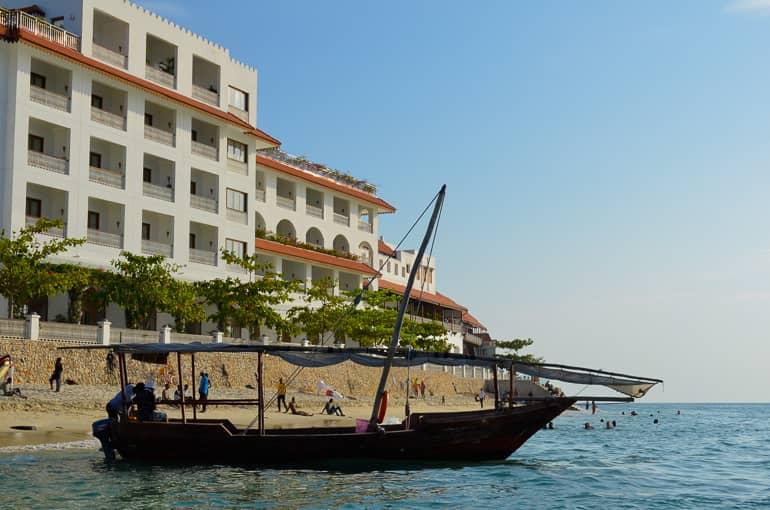 En la costa de un complejo hotelero en Zanzíbar, un dhow ha atracado, al fondo se ve a los bañistas en la playa.