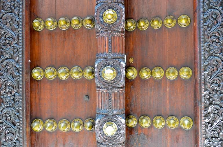 Una puerta decorada en Zanzíbar, Tanzania, con botones dorados y un pestillo igualmente ornamentado.