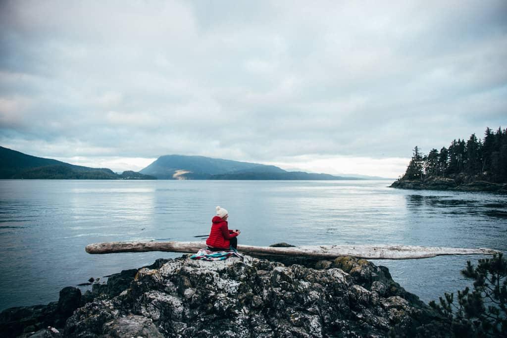 Vancouver Island: A woman in a red jacket sits on a rock overlooking the sea.