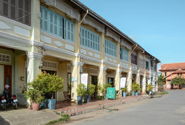 The arcades of the houses in Kampot have umbrellas and plants in front of them.