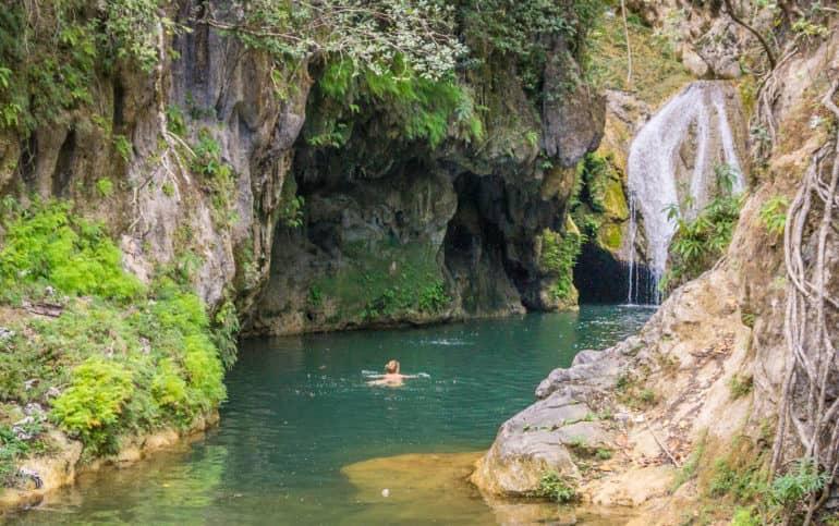 En Trinidad, Cuba, hay una cascada en el Parque el Cubano, a la que una mujer nada entre rocosos salientes.