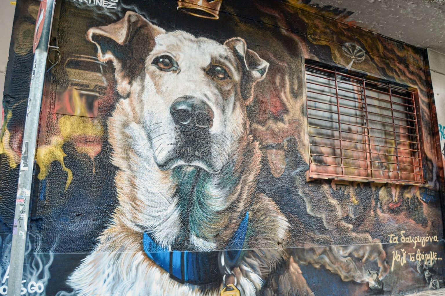 A large graffiti saying 'All Dogs go to Heaven' with the face of a dog on a wall in Athens.