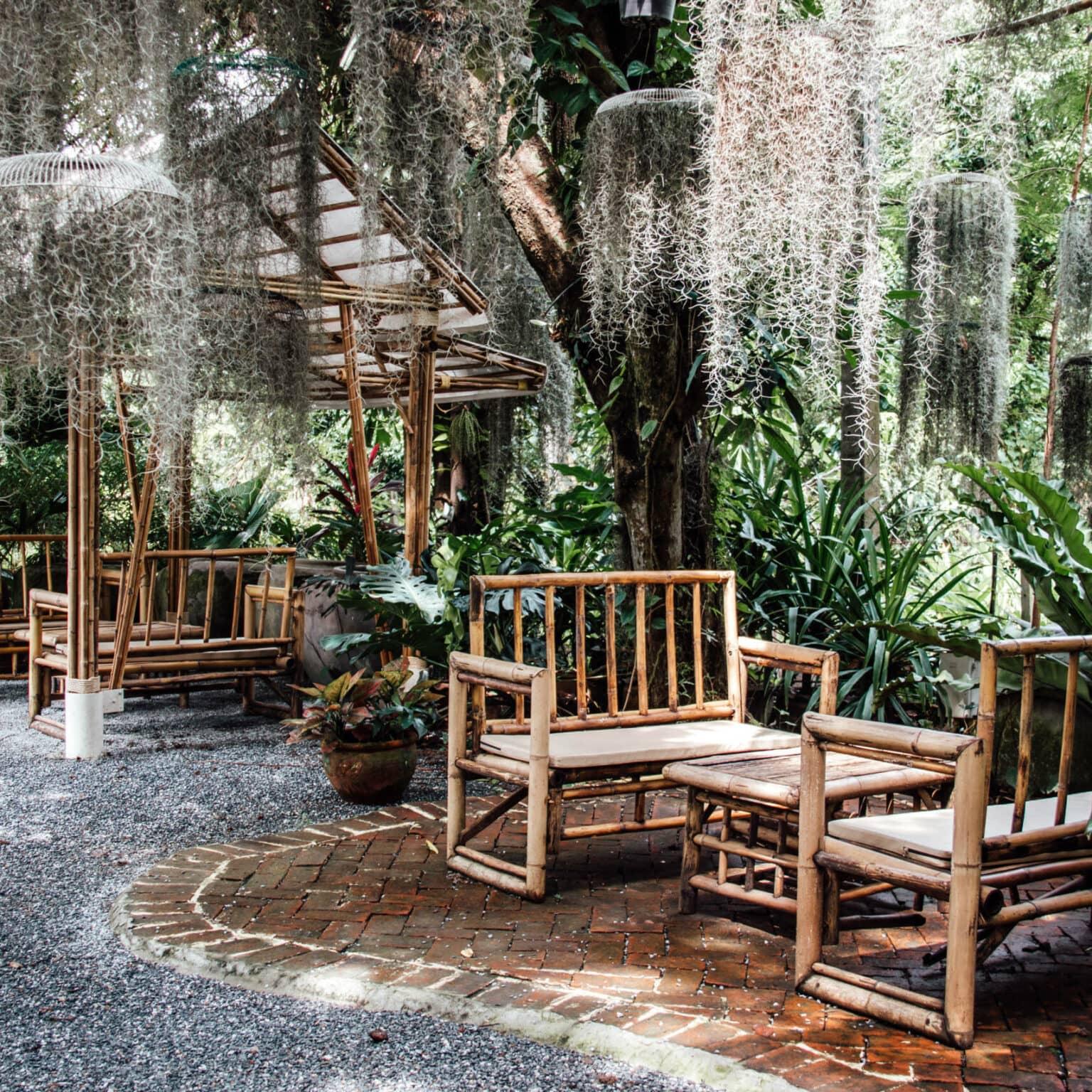 Bamboo benches and tables in Poomjai Garden surrounded by jungle-like plants.