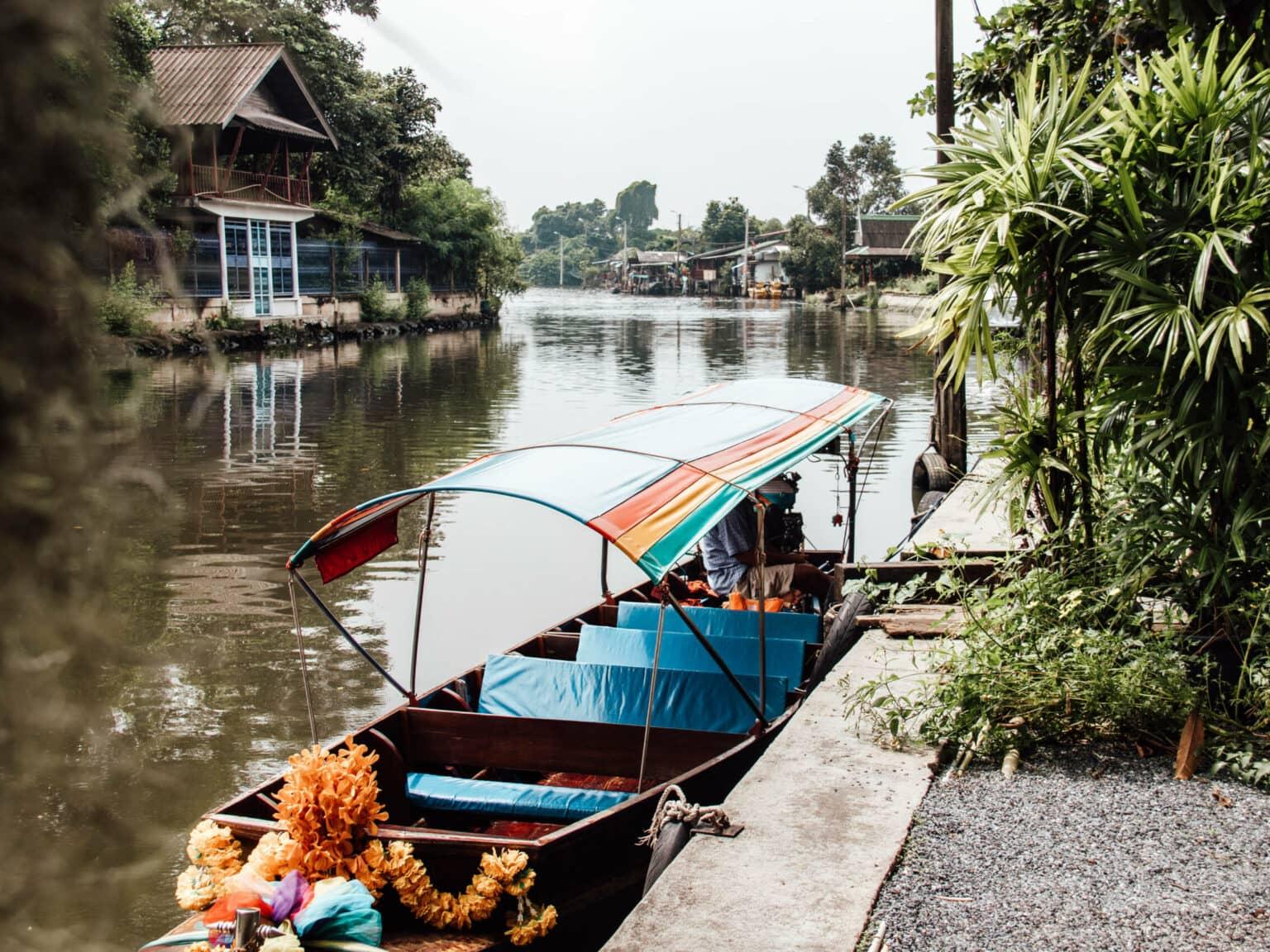 A longtail boat with a colorful tarp rests on the riverbank in Bangkok.