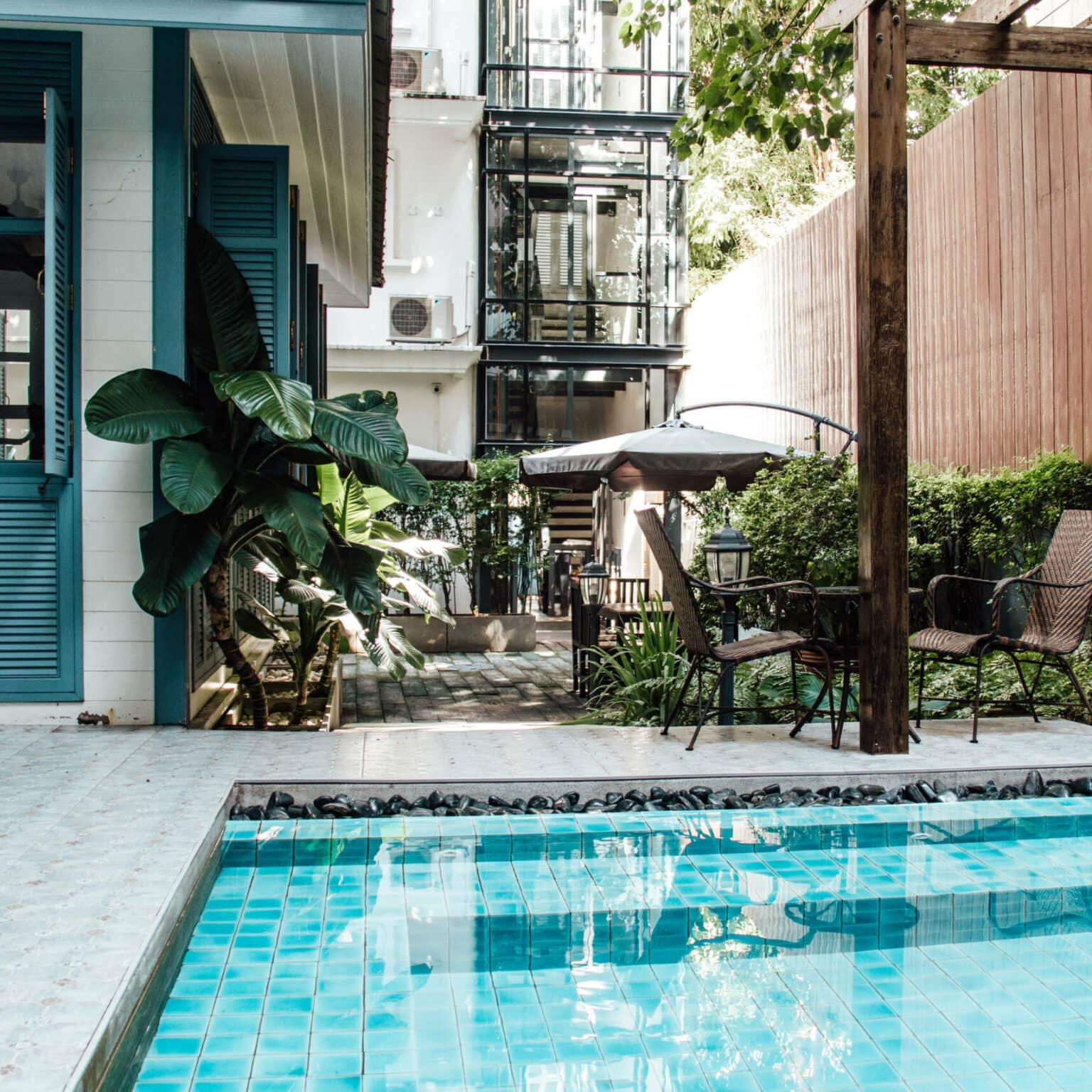 Jungle-like plants rise amidst a hotel with a pool.