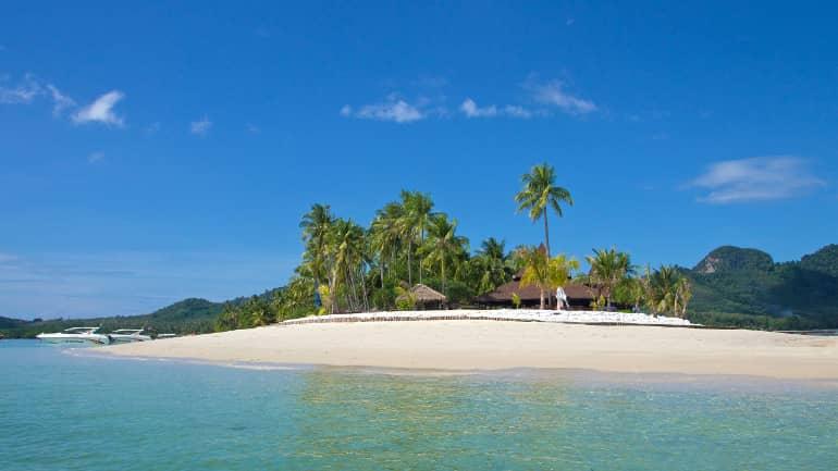 La península de Sivalai Beach en Koh Mook está rodeada de agua turquesa y playa de arena blanca, detrás de las palmeras se ve una cabaña de playa.