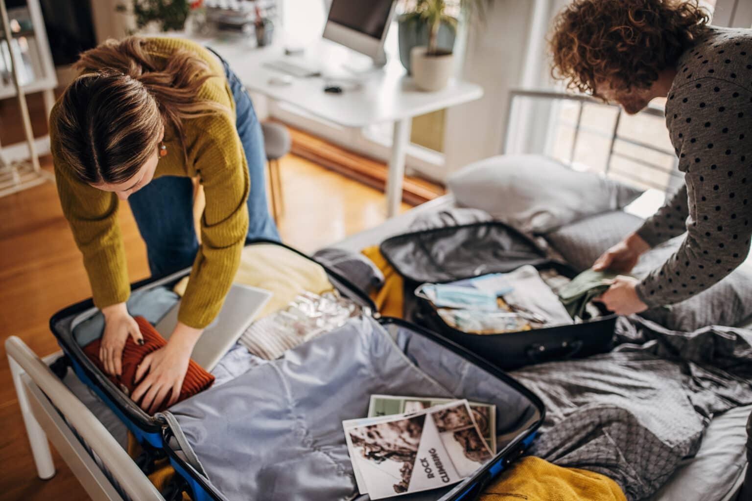 Dos personas empacando sus maletas en casa para las vacaciones.